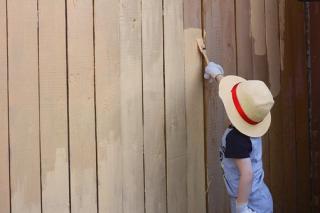 child in hat painting fence
